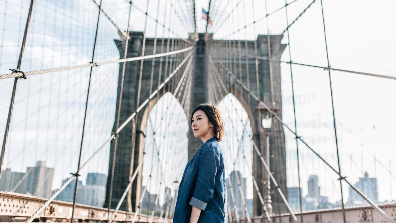 Young businesswoman looking up on Brooklyn Bridge against New York cityscape